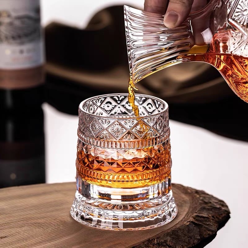 A person pouring whiskey into the rotating crystal glass