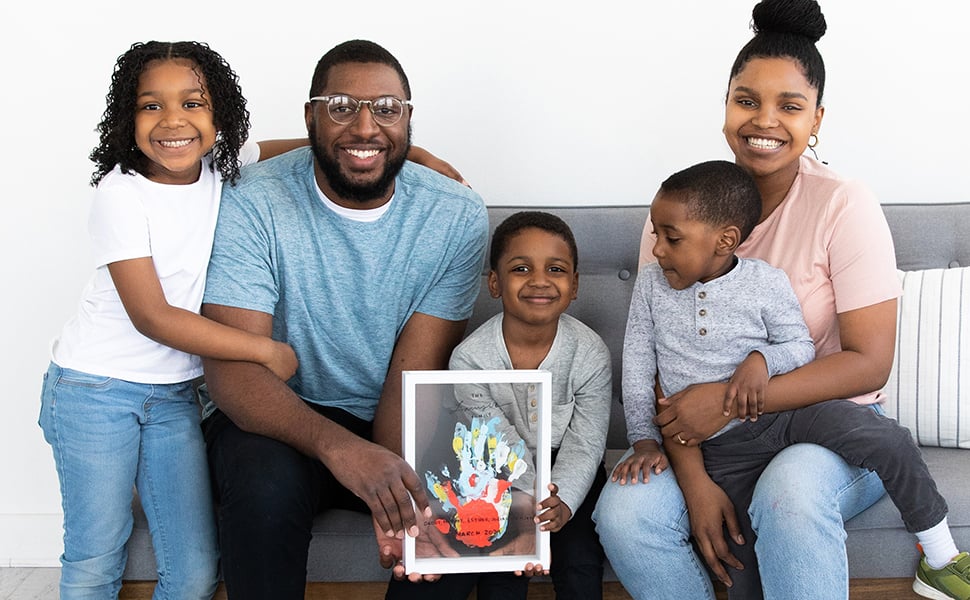 Family sitting on couch together and holding completed handprint frame Family sitting on couch together and holding completed handprint frame